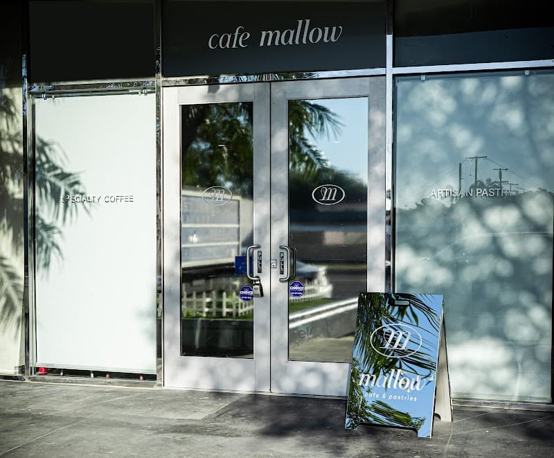 The real Cafe Mallow storefront in Downey, with palm shadows across its glass doors.