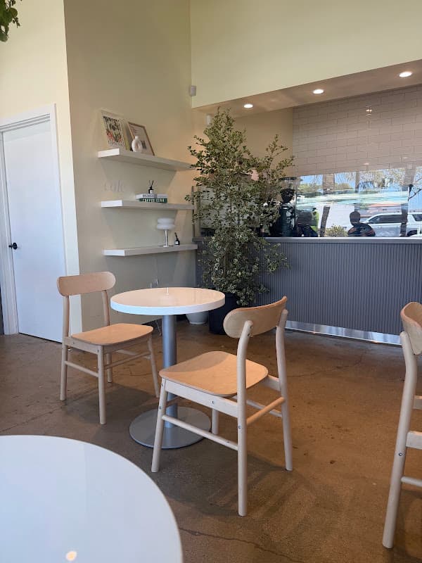 A sunlit corner of Cafe Mallow with pale wood chairs, a round table, and a green plant.